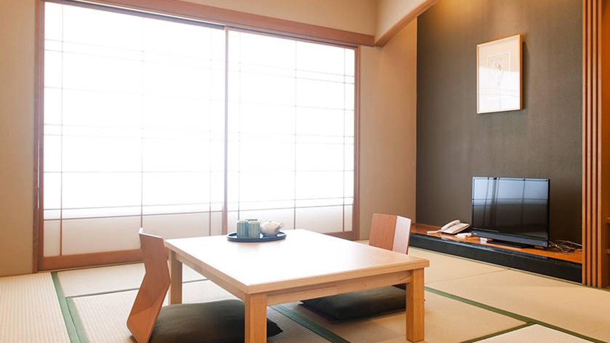 A traditional Japanese room with tatami flooring, a low table, a sofa, and a TV on a stand.