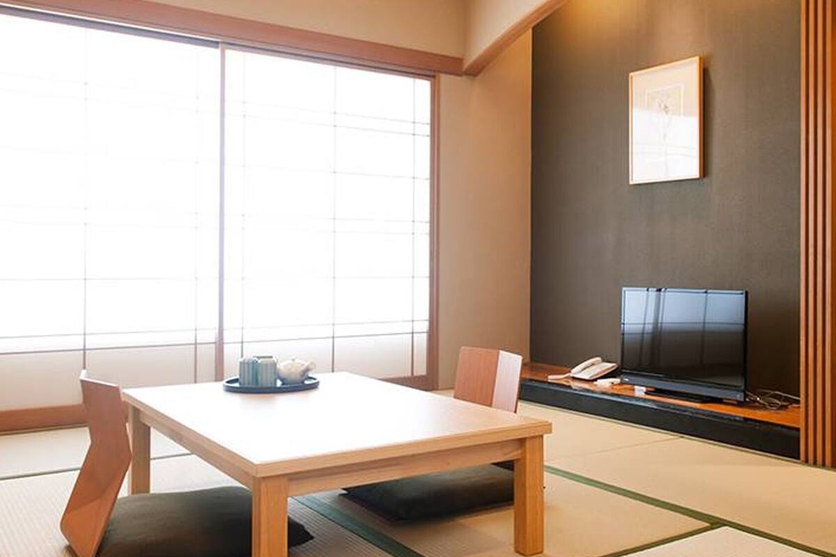 Um quarto japonês tradicional com tatames, uma mesa baixa, um sofá e uma TV sobre um suporte.