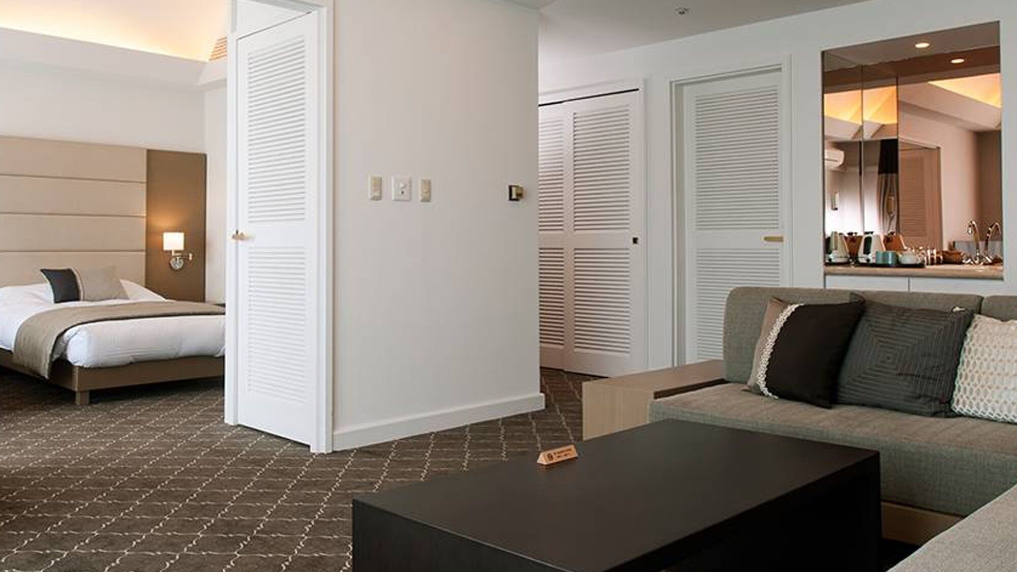 A hotel room with a bed, a sofa, a coffee table, and a mirror.