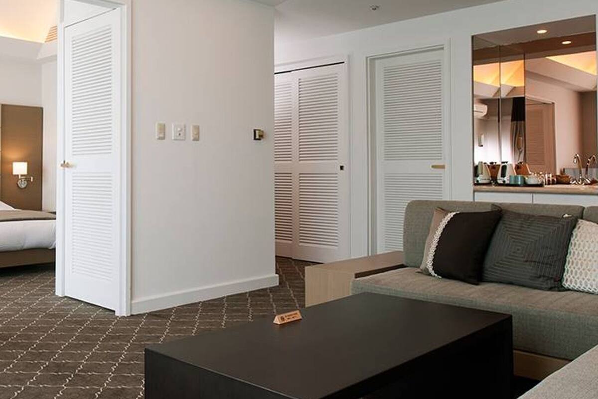 Quarto de hotel com cama, sofá, mesa de centro e espelho.