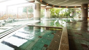 A large indoor swimming pool with clear water, surrounded by stone pillars and a glass barrier. - Sunhills Hotel (Utsunomiya)