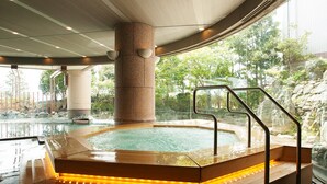 A hot tub with a wooden platform and steps, surrounded by a stone pillar and glass walls. - Sunhills Hotel (Utsunomiya)