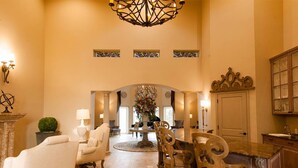 A spacious dining area with a round table and chairs, a chandelier, and a view through an arched doorway to another room. - Sunhills Hotel (Utsunomiya)