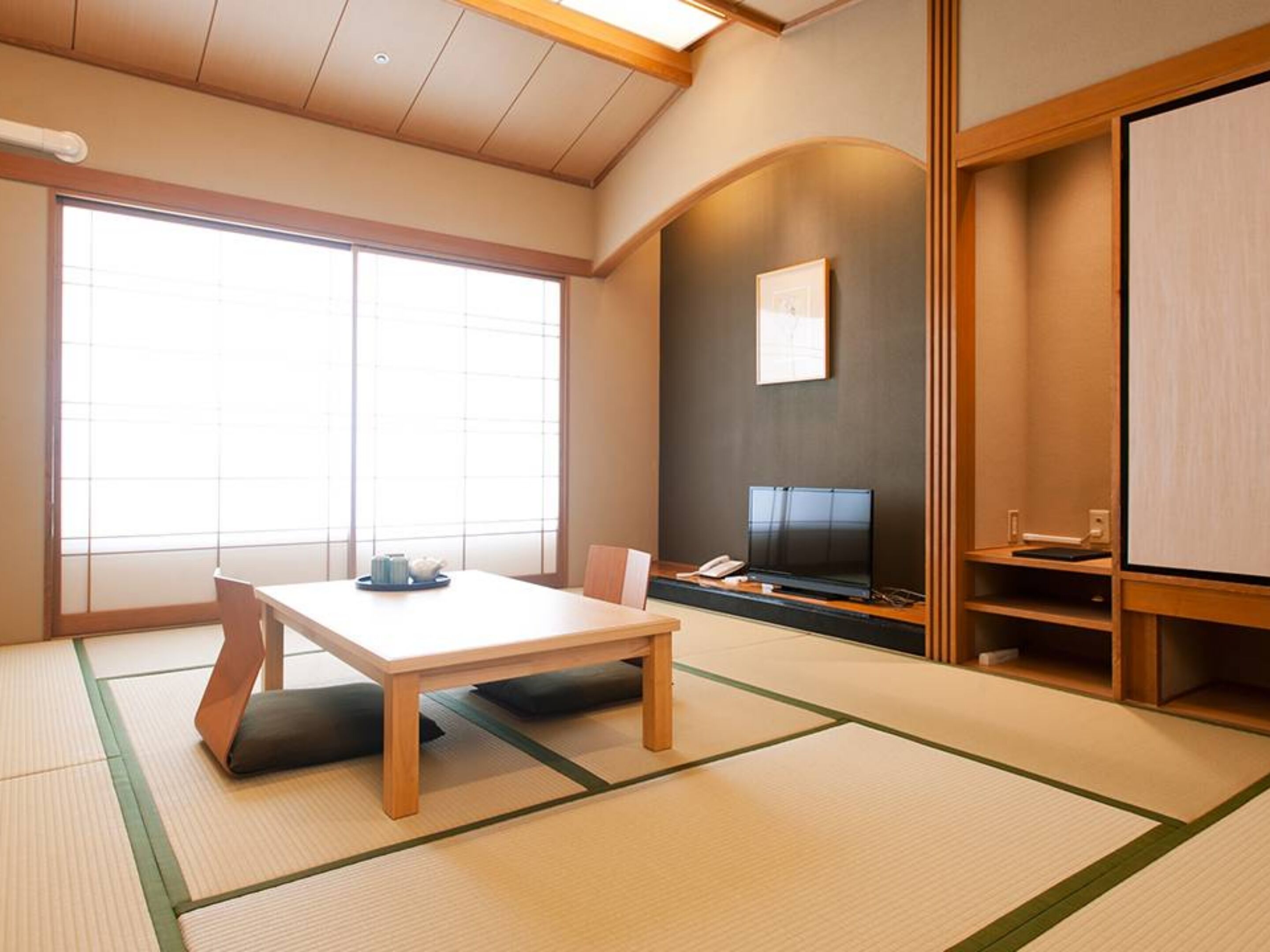 Una habitación japonesa tradicional con suelo de tatami, una mesa baja, un televisor y una puerta corredera.