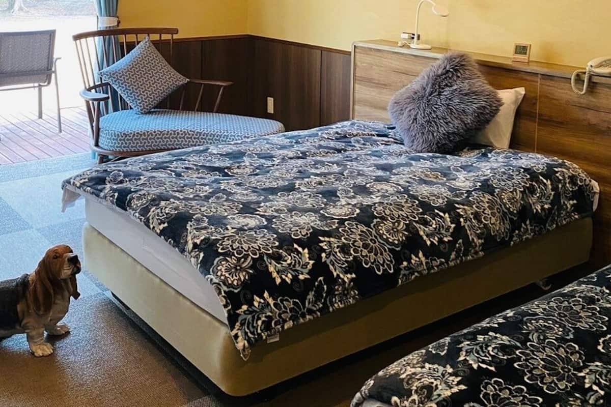 A bedroom with a bed, a chair, a small table, and a dog.