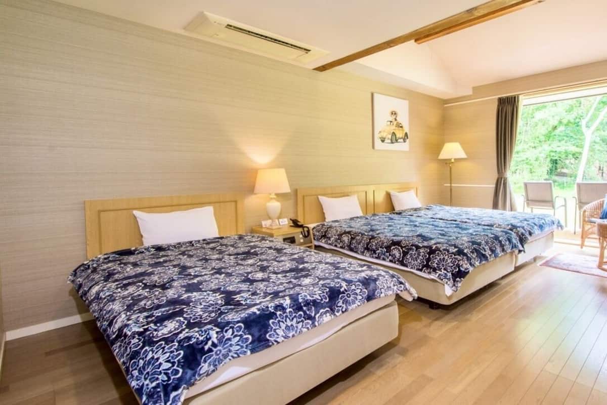 A hotel room with two beds, a sofa, a table, and a view of the outdoors.