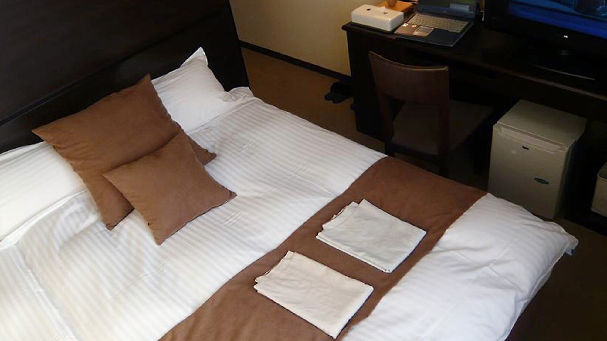 A hotel room with a bed, a desk with a laptop, and a small cabinet.