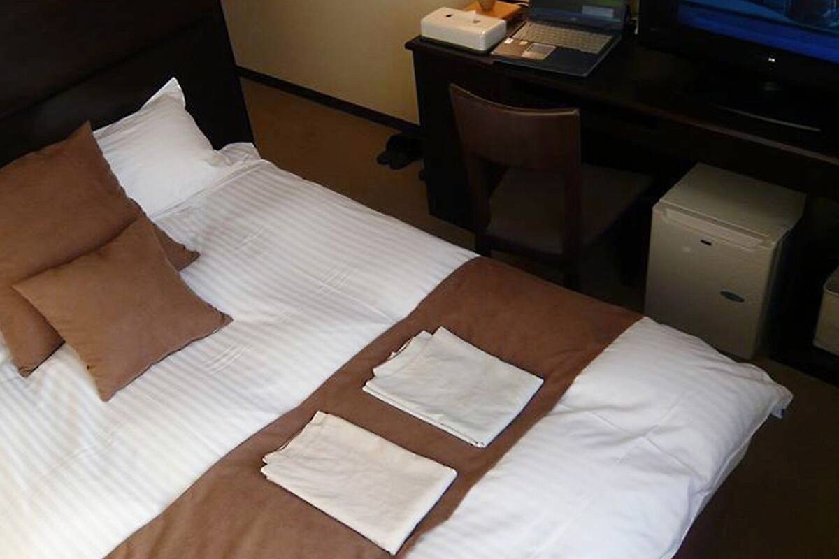 Una habitación de hotel con una cama, un escritorio con una computadora portátil y un mueble bajo.