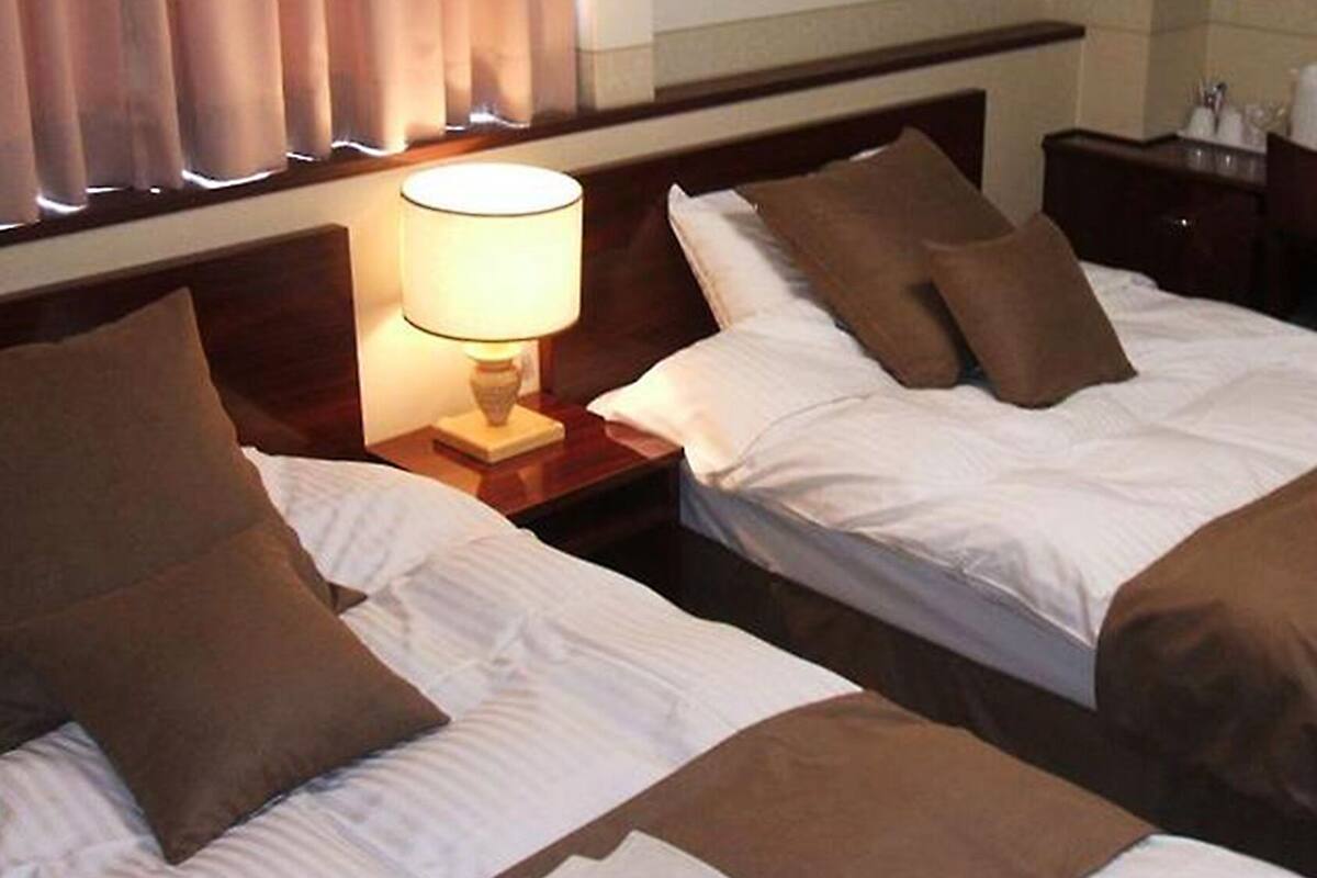 Una habitación de hotel con dos camas, una mesita de noche con lámpara y un aparador con artículos de aseo.