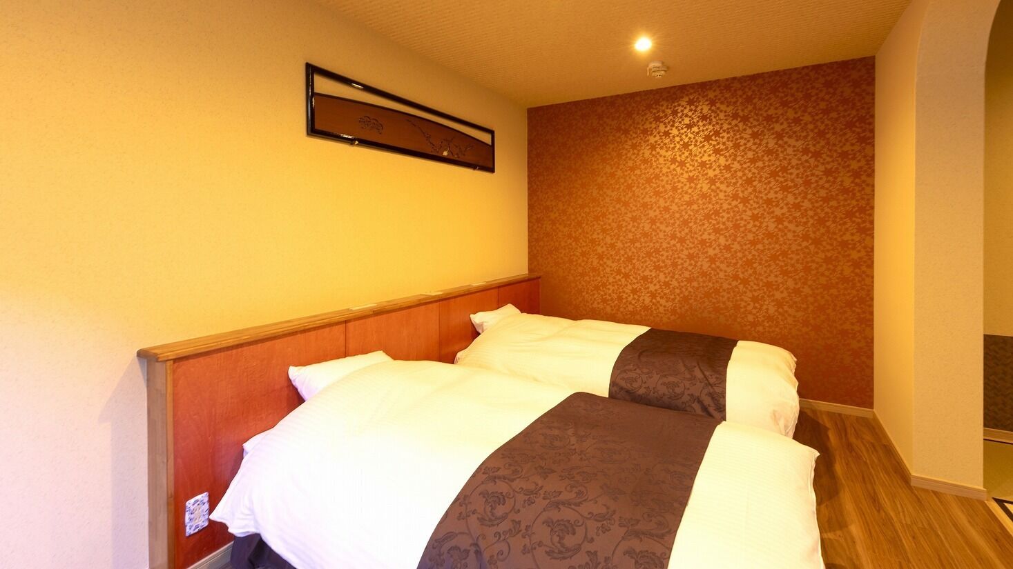 A hotel room with a bed, a wooden headboard, a patterned wall, and a ceiling light.