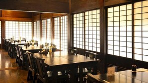 Ein Restaurant mit mehreren Tischen und Stühlen, großen Fenstern und einer Holzvertäfelung.