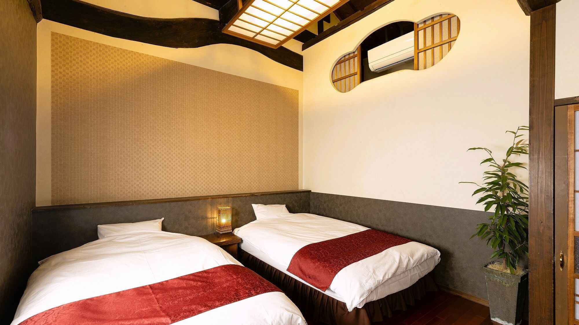 A hotel room with two beds, a large window, and a plant.