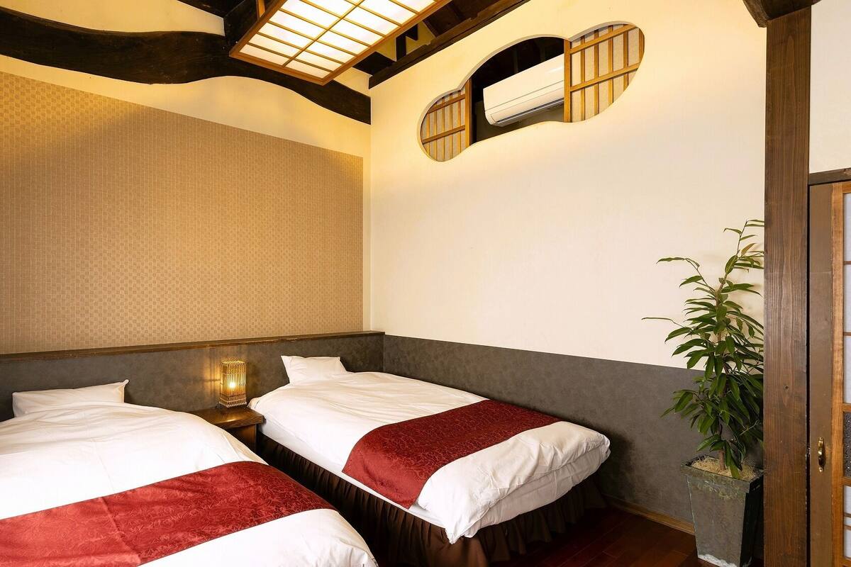 A hotel room with two beds, a large window, and a plant.