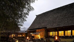 Ein traditionelles japanisches Gebäude mit einem strohgedeckten Dach, Steinlaternen und einem hölzernen Eingang.