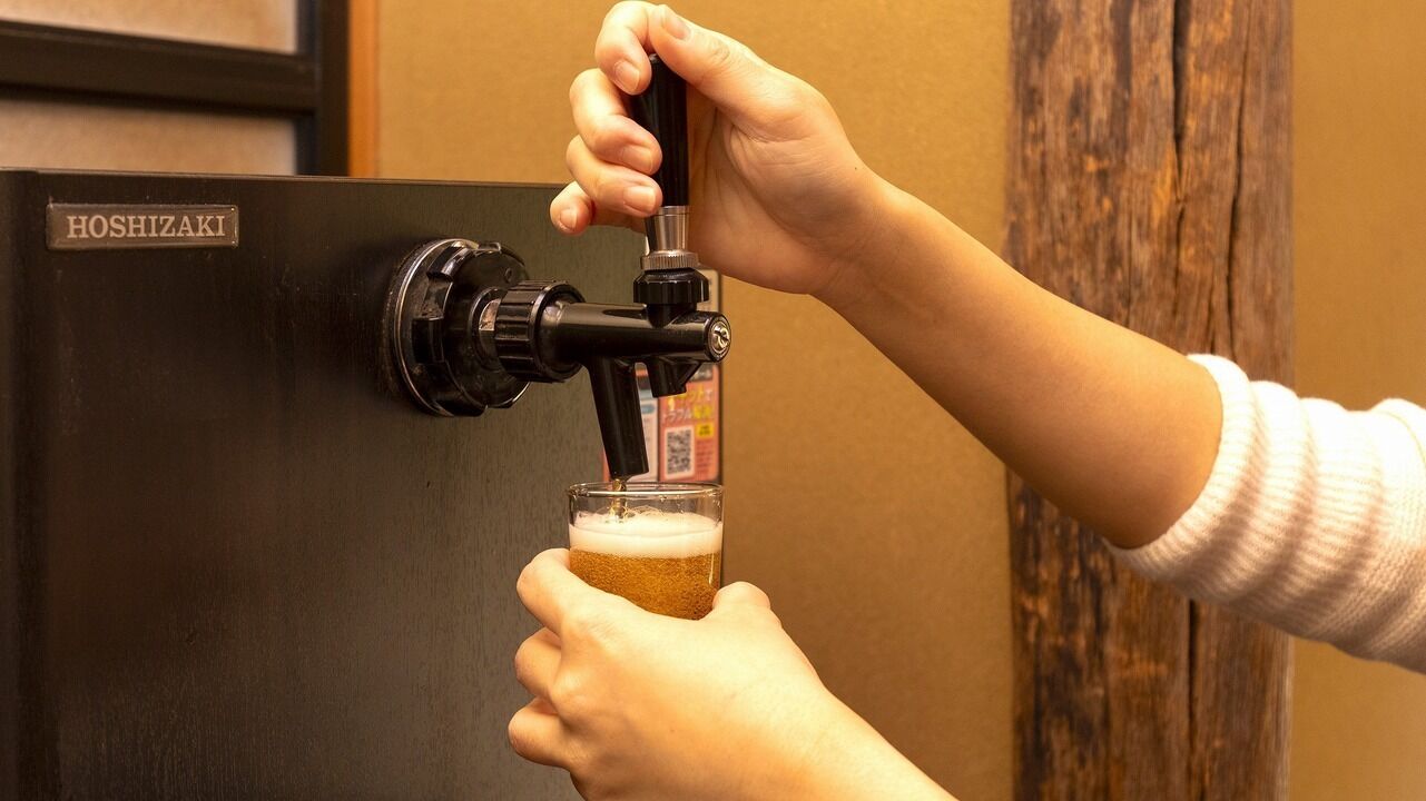 A person pouring beer from a tap labeled 'HOSHIZAKI' into a glass.
