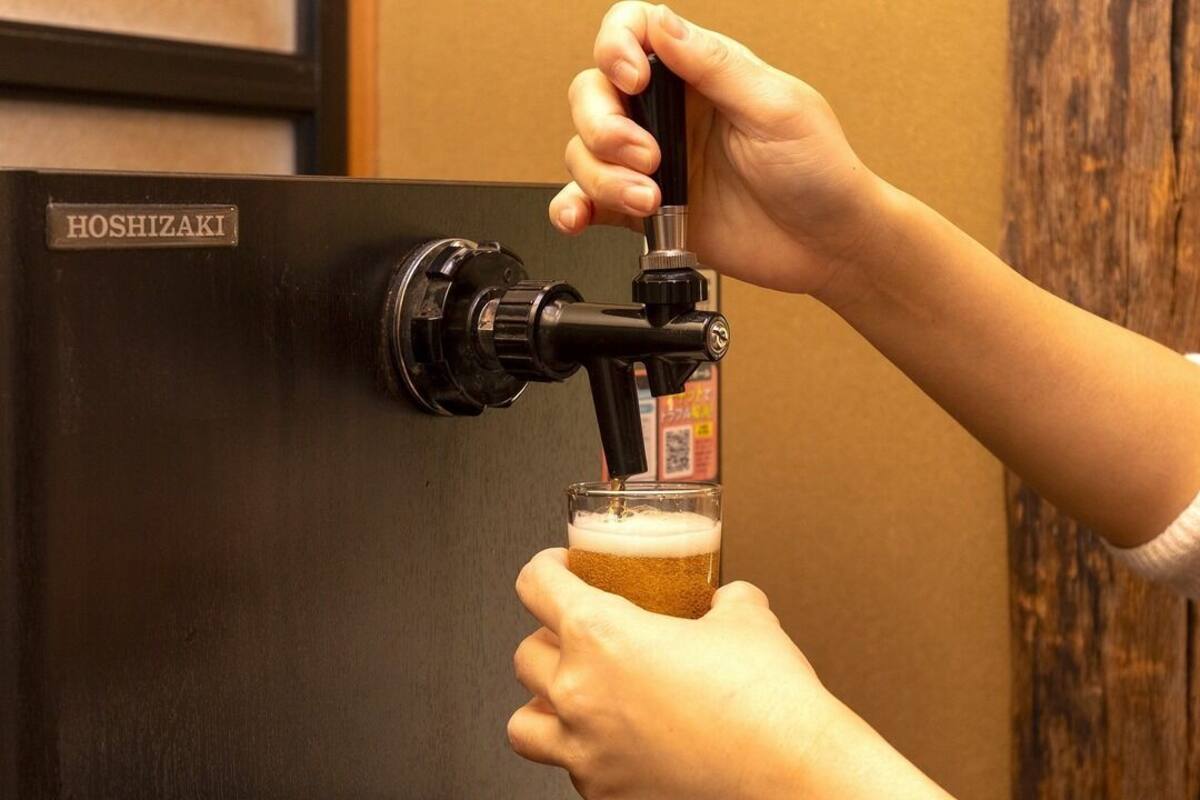 A person pouring beer from a tap labeled 'HOSHIZAKI' into a glass.