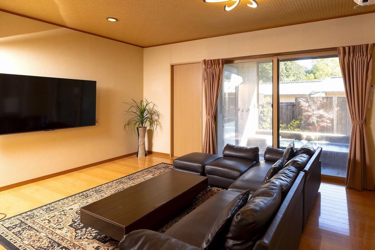 A living room with a sofa set, a flat-screen TV, a potted plant, and a sliding glass door leading to an outdoor area.