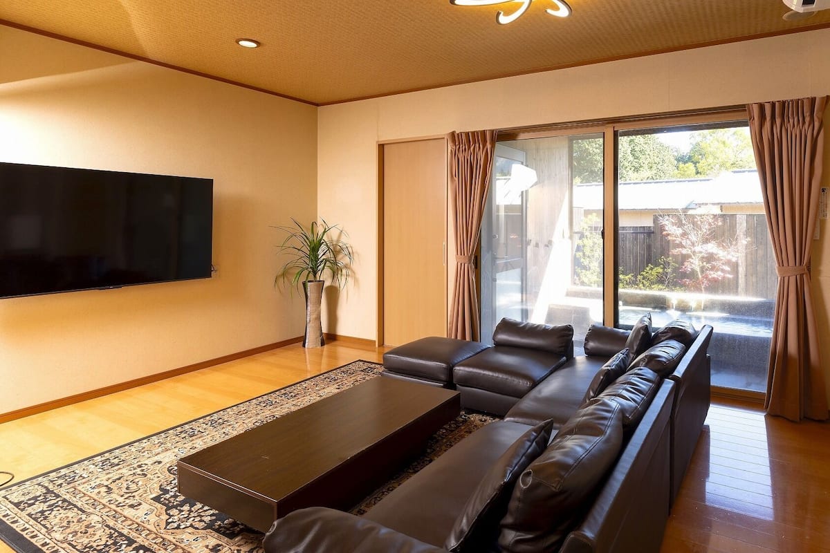 A living room with a sofa set, a flat-screen TV, a potted plant, and a sliding glass door leading to an outdoor area.