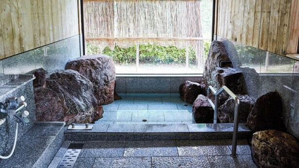 A stone-walled bathroom with a shower area, large rocks, and a window overlooking greenery. - Hosenbo Lodge (Seiyo)