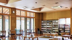 A library with wooden tables and chairs, bookshelves, and large windows. - Hosenbo Lodge (Seiyo)