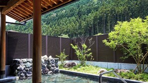 A spa area with a stone pool, wooden pergola, and a view of a forested hillside. - Hosenbo Lodge (Seiyo)
