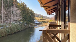 A wooden deck overlooking a river with a view of trees and hills. - Hosenbo Lodge (Seiyo)