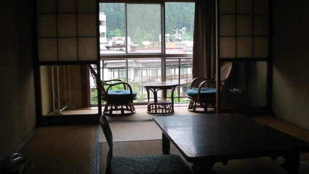 A traditional Japanese room with tatami flooring, a low table, and two chairs. - Miharaya Ryokan (Gujo)