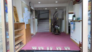 A hallway with a pink carpet, a wooden shoe rack, and a staircase. - Miharaya Ryokan (Gujo)