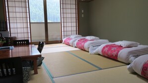 A traditional Japanese room with tatami flooring, a low table with chairs, and a bed with pink floral bedding. - Miharaya Ryokan (Gujo)