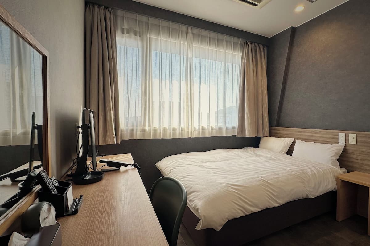 Habitación de hotel con una cama grande, un escritorio con una computadora, una silla y una ventana con cortinas.