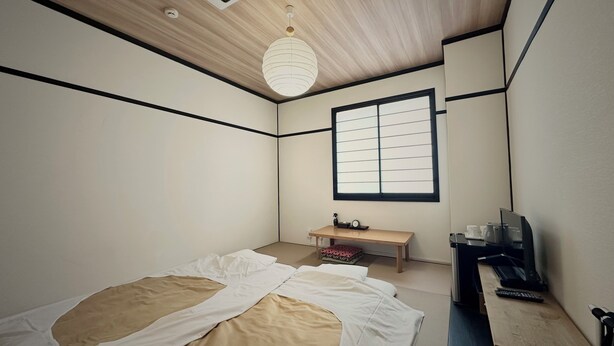 A bedroom with a bed, a desk, a chair, a window, and a ceiling light. - Hotel Sunroad (Amakusa)