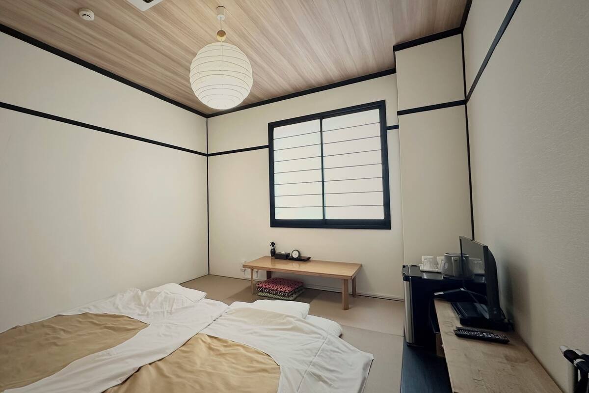 A bedroom with a bed, a desk, a chair, a window, and a ceiling light.
