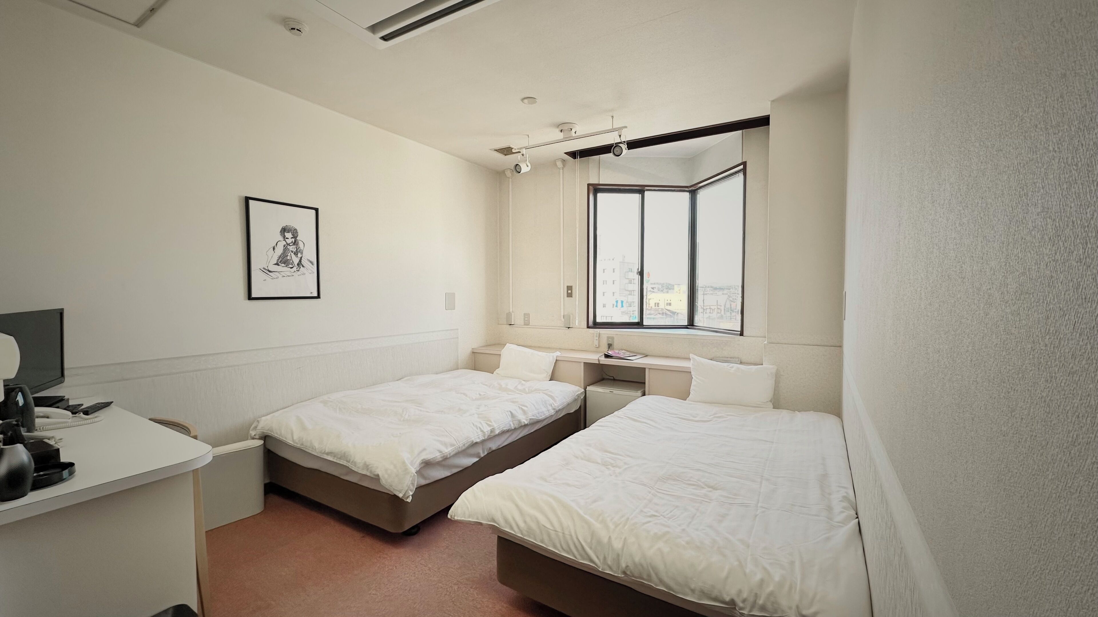 A small, clean room with two beds, a desk, and a window.