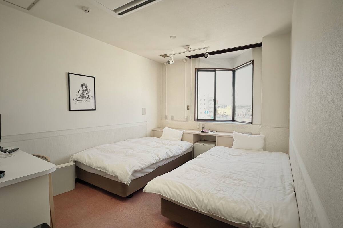 A small, clean room with two beds, a desk, and a window.