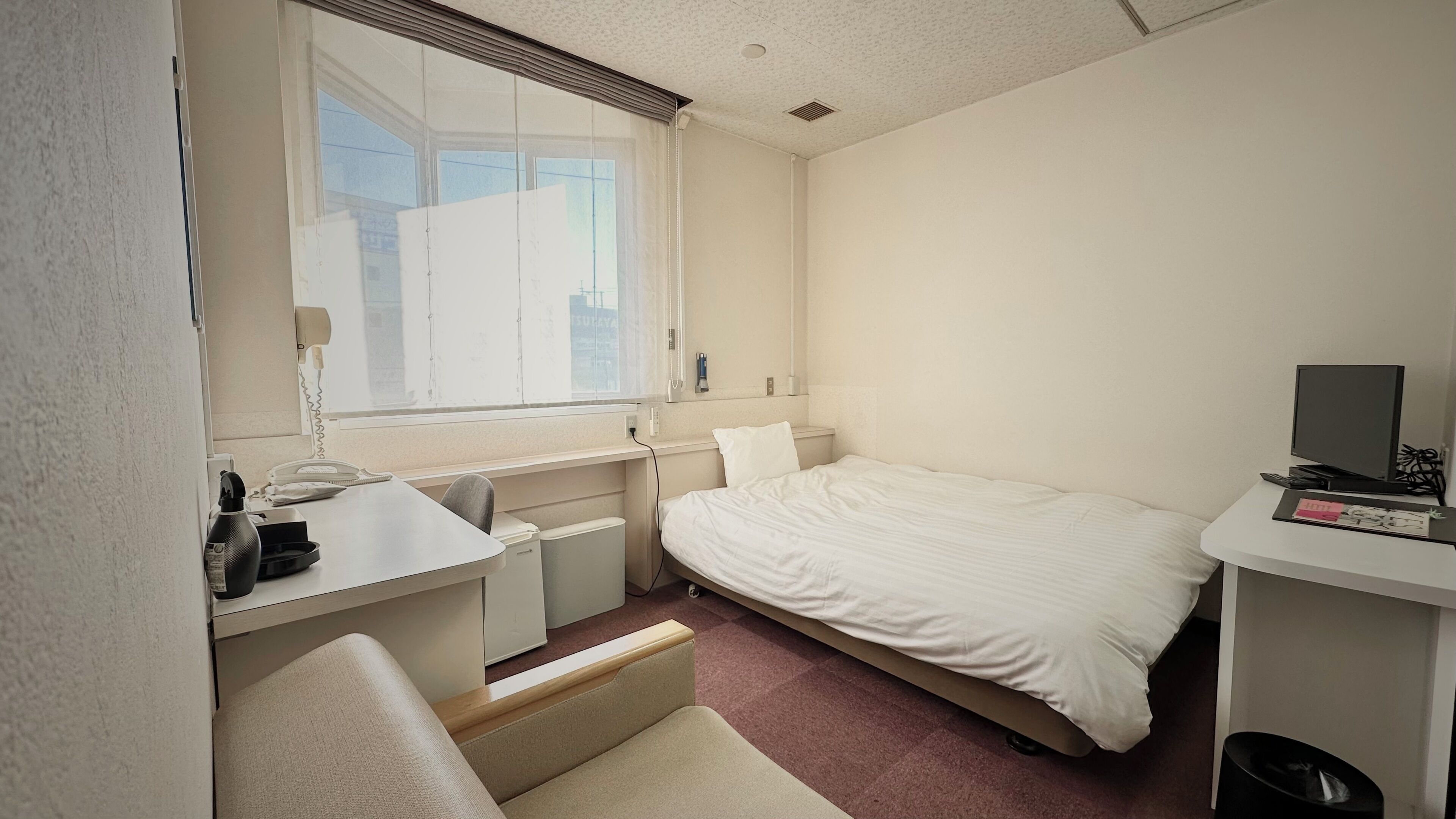 A hotel room with a bed, a desk, a chair, a TV, and a window with blinds.