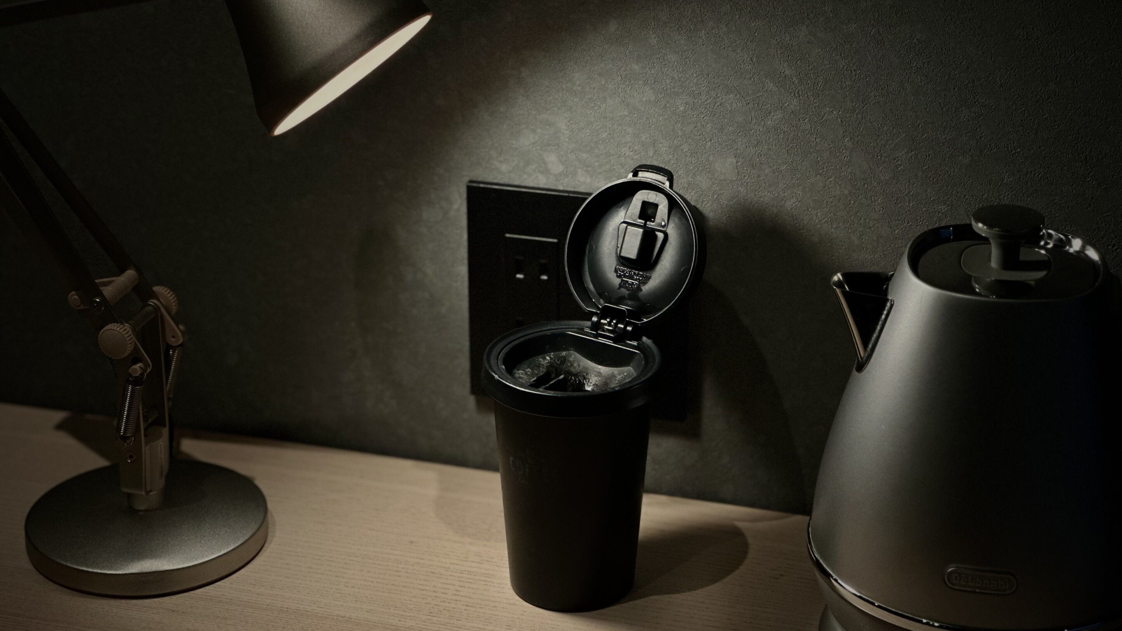 A desk with a coffee maker, a cup, and a lamp.