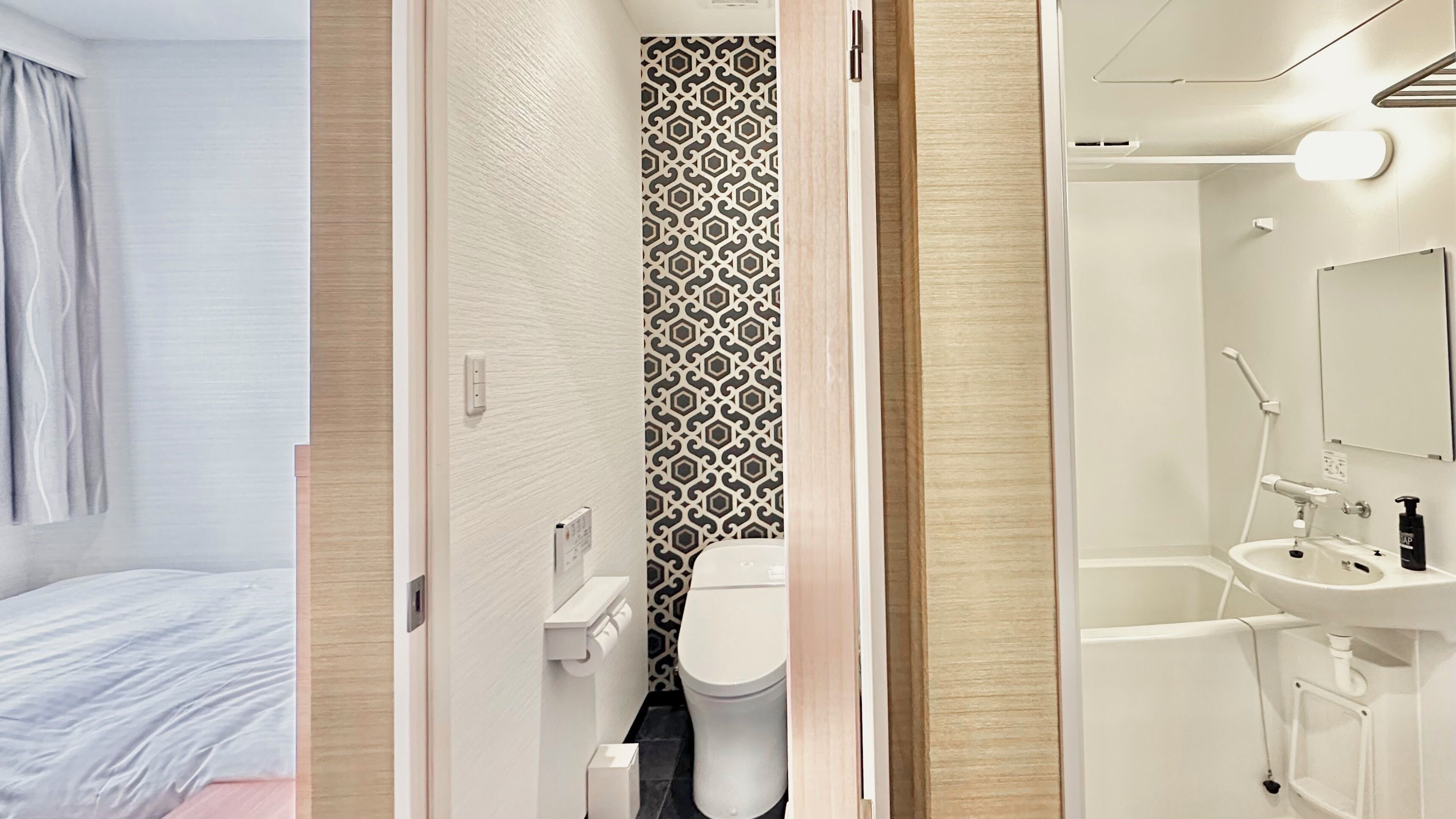 Un baño moderno con inodoro, lavamanos y ducha. Presenta una pared con un diseño y una puerta de madera.