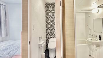 Un baño moderno con inodoro, lavamanos y ducha. Presenta una pared con un diseño y una puerta de madera.