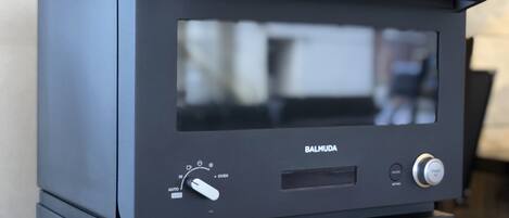 A black Balmuda oven with a control panel, placed on a wooden surface.