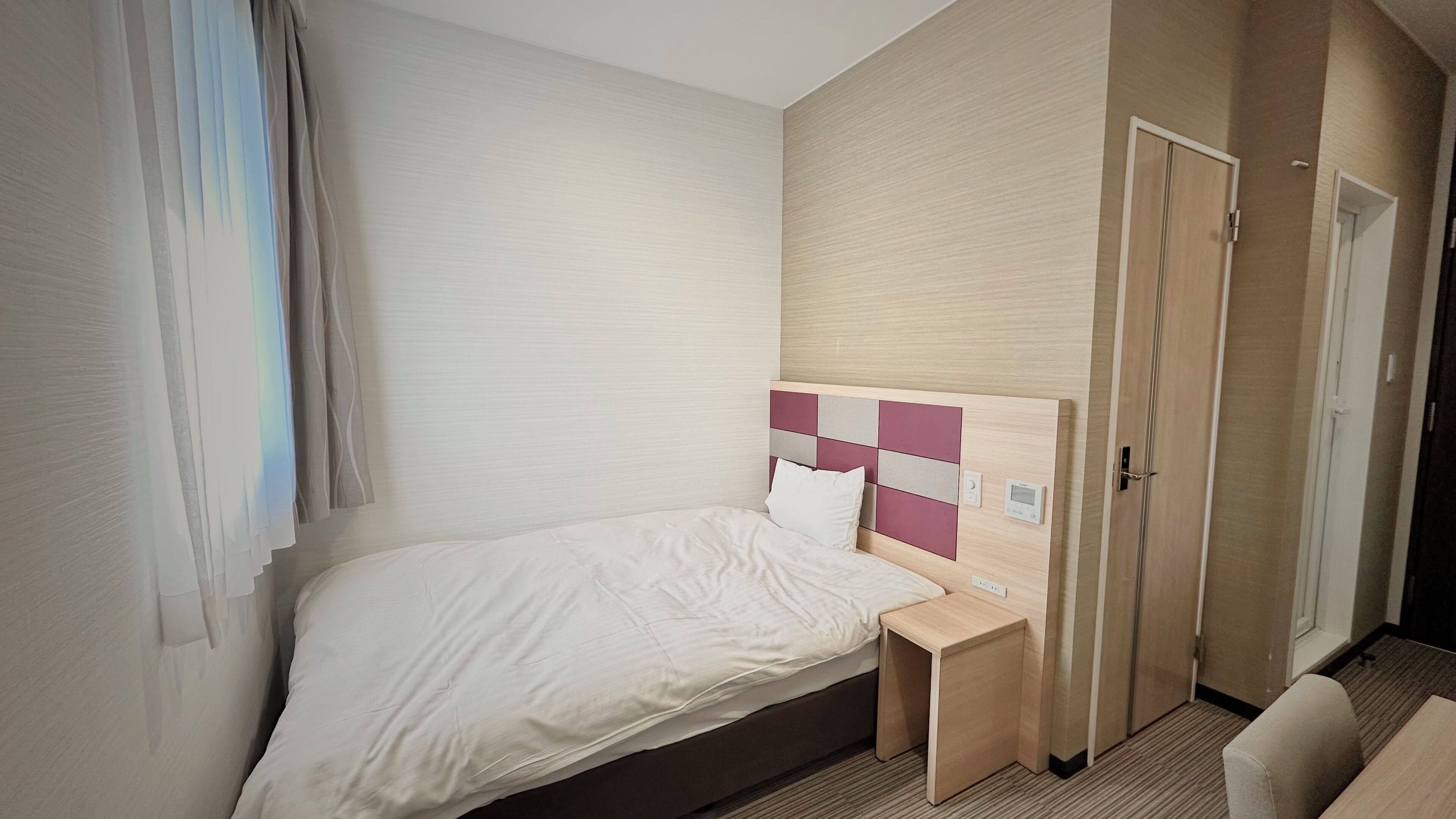 A hotel room with a bed, bedside table, and a wardrobe.