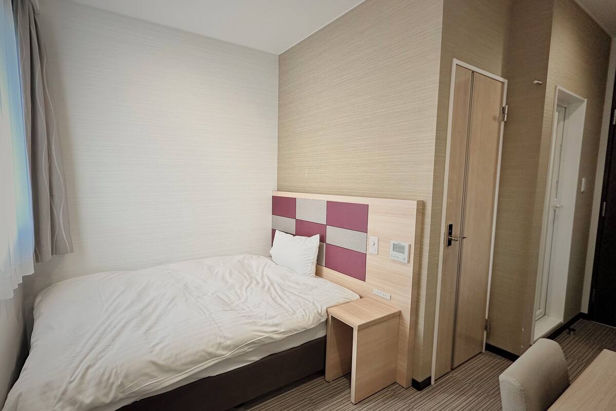 A hotel room with a bed, bedside table, and a wardrobe.