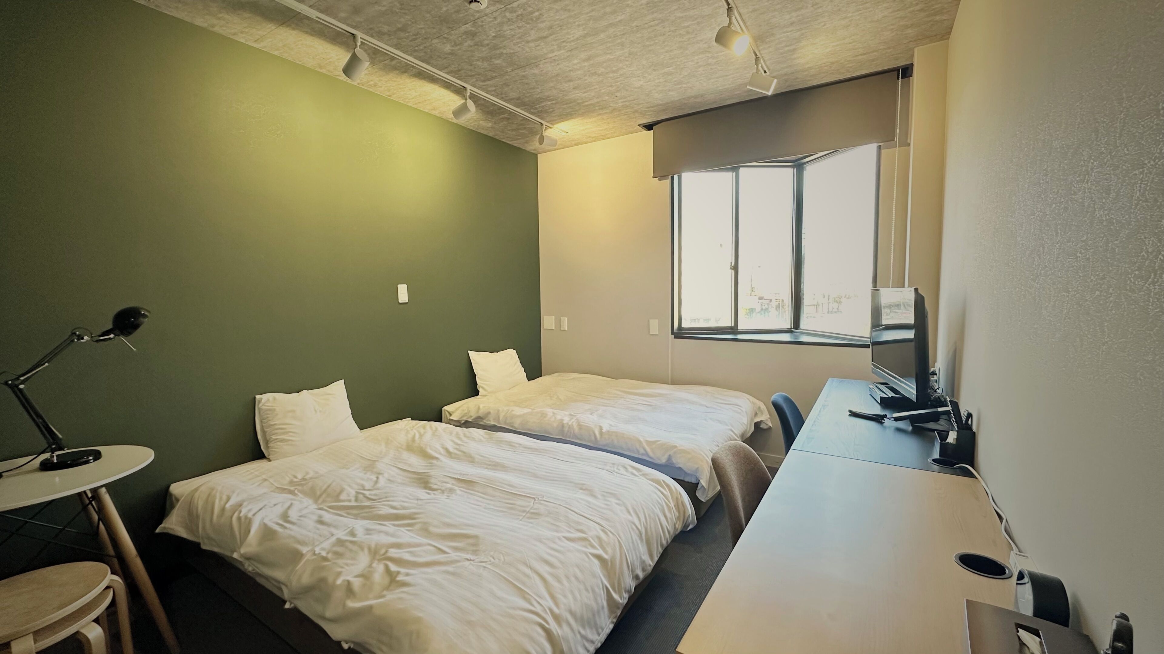 A small, clean room with two beds, a desk, and a window.