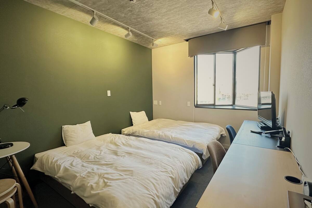 A small, clean room with two beds, a desk, and a window.