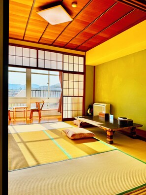 Une pièce de style japonais traditionnel, avec un sol recouvert de tatamis, une table basse, des chaises, une porte coulissante et une vue sur l’extérieur.