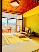 A traditional Japanese room with tatami flooring, a low table, chairs, a sliding door, and a view of the outside.