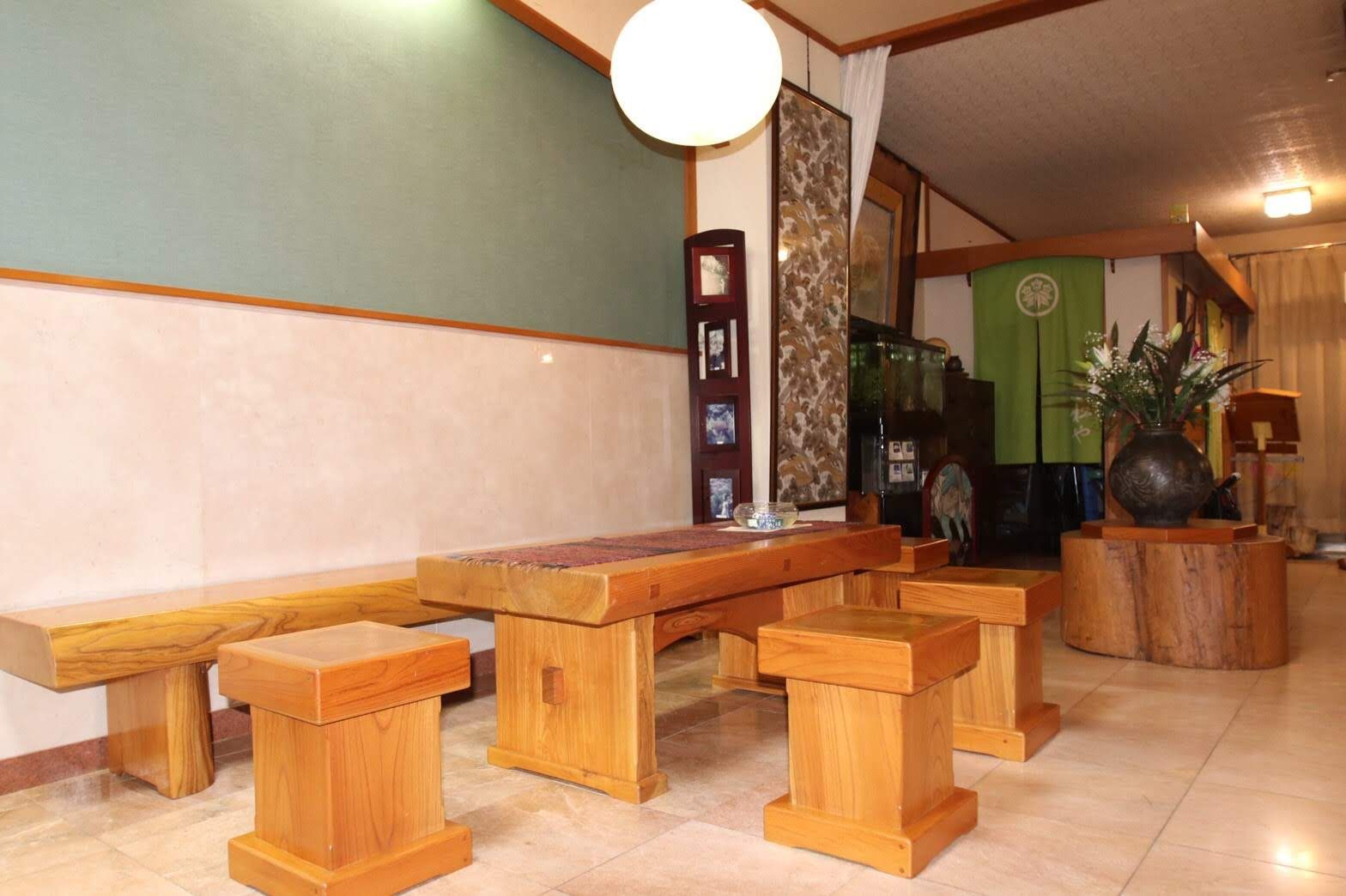 Een zithoek met houten bankje, een tafel, een decoratieve vaas en een muur met een klok en ingelijste foto's.