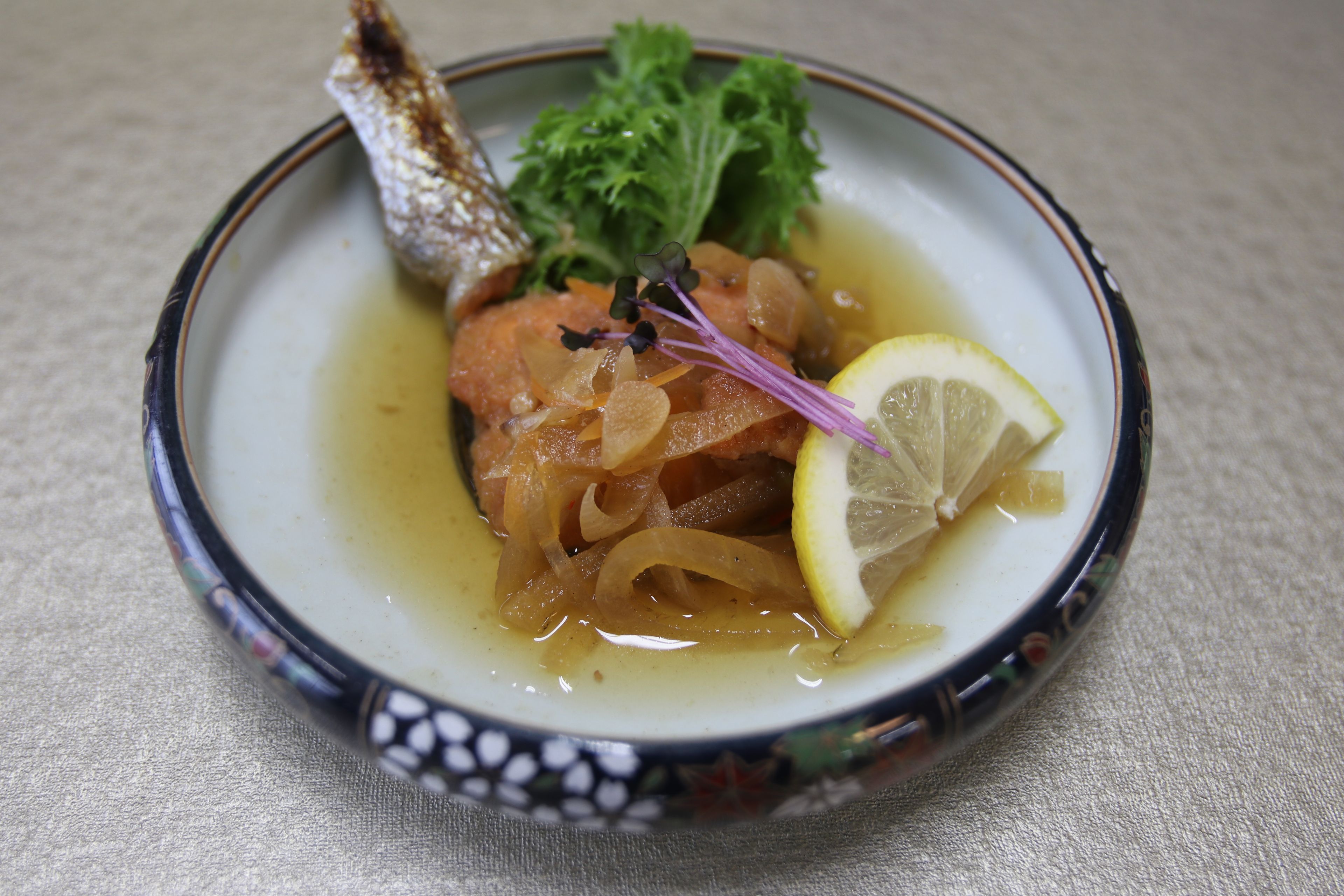 A plate with a fish, lemon, and greens.
