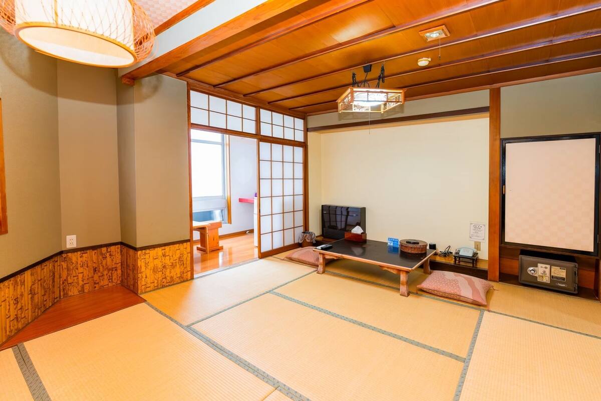 Una habitación japonesa tradicional con suelo de tatami, una mesa baja, televisor y puertas correderas.