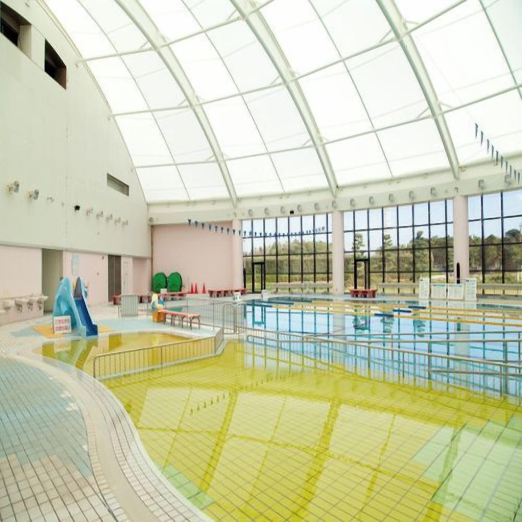 Una piscina interior con techo de vidrio, varias pistas de natación y un tobogán.