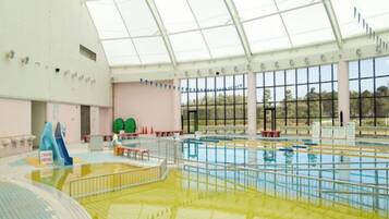 Una piscina interior con techo de vidrio, varias pistas de natación y un tobogán.